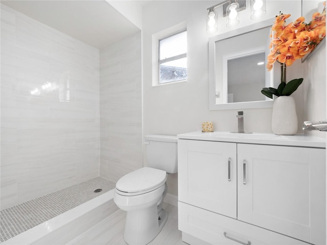 bathroom with tiled shower, vanity, and toilet