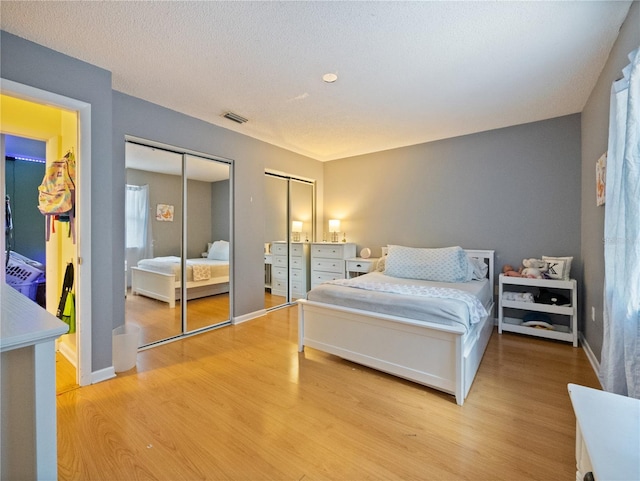 bedroom with light hardwood / wood-style flooring, two closets, and a textured ceiling