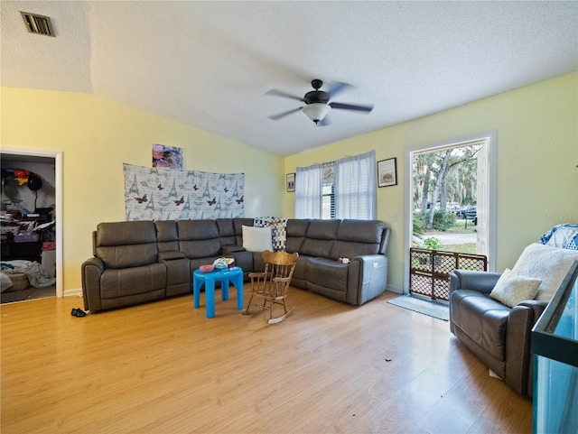 living room with light hardwood / wood-style flooring, lofted ceiling, ceiling fan, and a textured ceiling