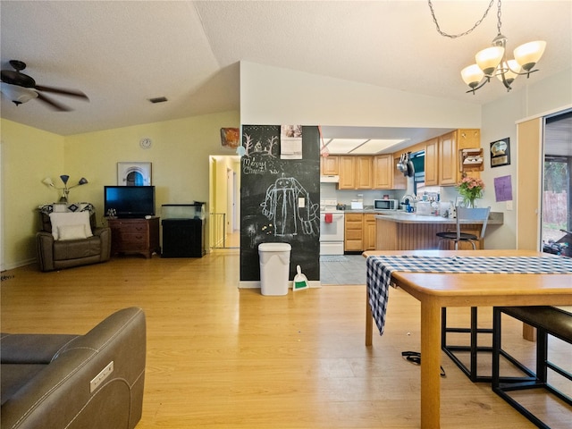 dining space with light hardwood / wood-style flooring, vaulted ceiling, and ceiling fan with notable chandelier