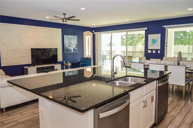 kitchen with white cabinetry, a kitchen island with sink, dark stone counters, stainless steel dishwasher, and sink