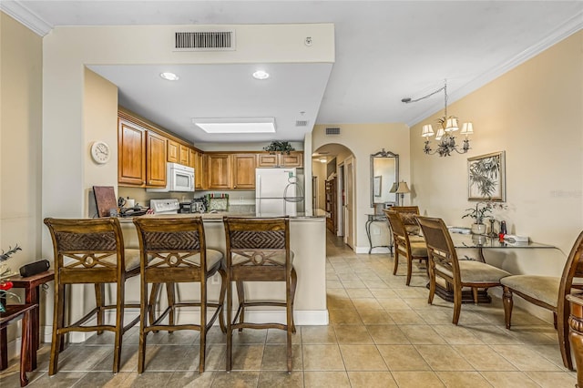 kitchen with white appliances, a chandelier, kitchen peninsula, and a kitchen breakfast bar