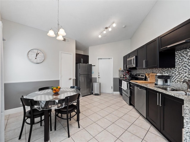 kitchen featuring backsplash, light stone countertops, stainless steel appliances, decorative light fixtures, and sink