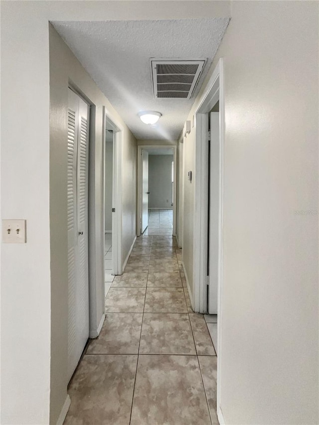 hallway with a textured ceiling and light tile patterned flooring