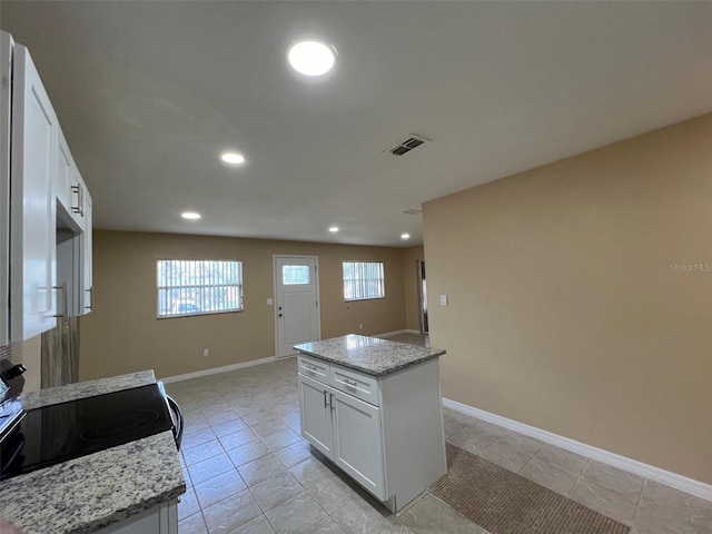 kitchen featuring light stone countertops, white cabinets, a center island, and range