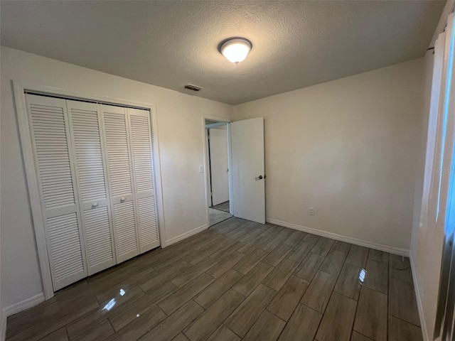 unfurnished bedroom featuring a textured ceiling, a closet, and dark hardwood / wood-style floors