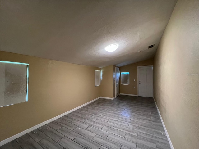 empty room featuring lofted ceiling, light hardwood / wood-style floors, and a textured ceiling