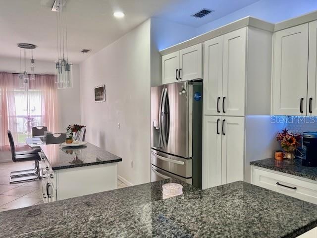 kitchen with white cabinets, stainless steel refrigerator with ice dispenser, a center island, and dark stone countertops