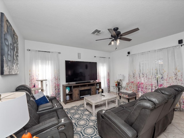 living room featuring a fireplace, a textured ceiling, ceiling fan, and light tile patterned flooring