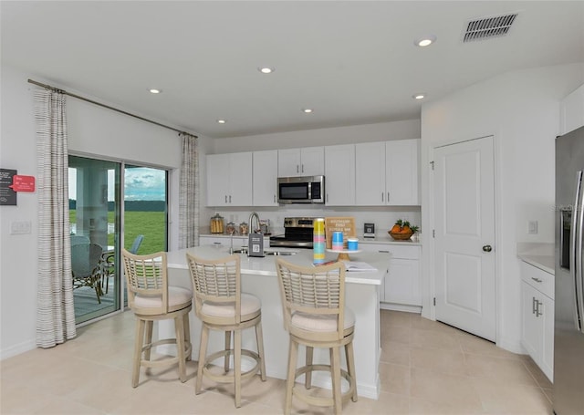 kitchen featuring appliances with stainless steel finishes, light tile patterned flooring, white cabinets, a kitchen bar, and a center island with sink