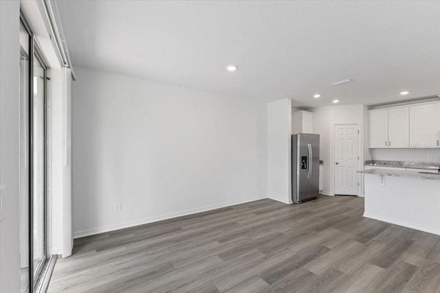 kitchen with light stone countertops, stainless steel fridge with ice dispenser, light wood-type flooring, and white cabinetry