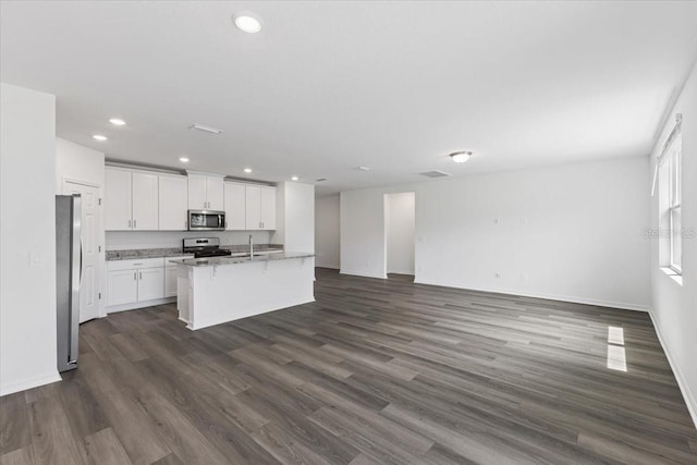 kitchen with white cabinetry, light stone counters, dark hardwood / wood-style flooring, a center island with sink, and appliances with stainless steel finishes