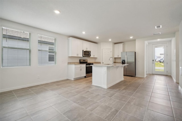 kitchen with light stone countertops, appliances with stainless steel finishes, sink, a center island with sink, and white cabinetry