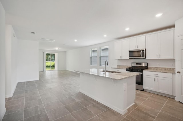 kitchen featuring white cabinetry, sink, stainless steel appliances, light stone counters, and a kitchen island with sink