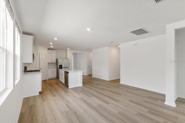 kitchen featuring stainless steel appliances, decorative backsplash, a center island with sink, white cabinets, and light wood-type flooring