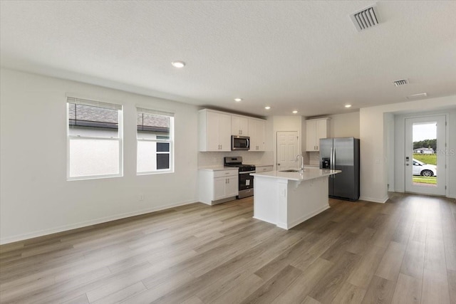 kitchen with appliances with stainless steel finishes, sink, light hardwood / wood-style floors, white cabinetry, and an island with sink