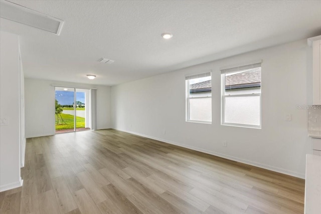 spare room with a textured ceiling, light hardwood / wood-style flooring, and a wealth of natural light