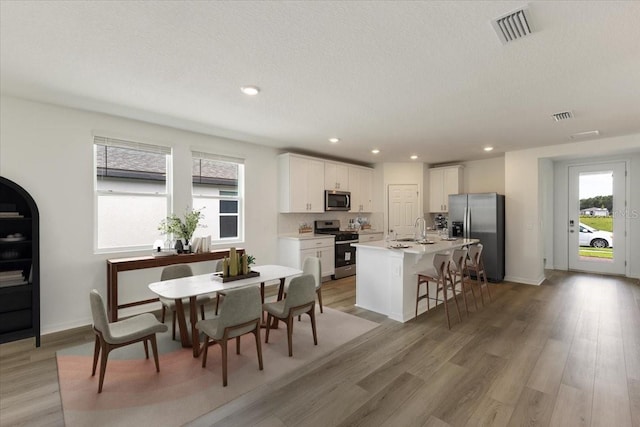 kitchen featuring appliances with stainless steel finishes, a kitchen breakfast bar, sink, white cabinetry, and an island with sink