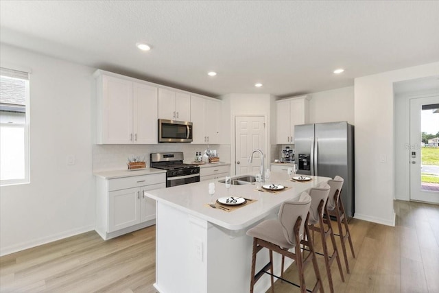 kitchen with an island with sink, sink, white cabinets, and stainless steel appliances