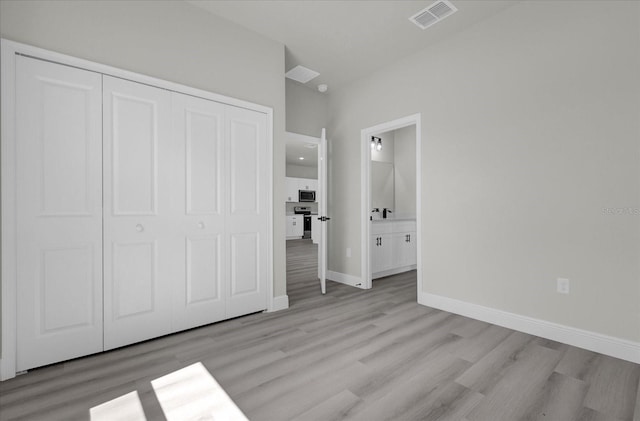 unfurnished bedroom with ensuite bathroom, a closet, and light hardwood / wood-style flooring