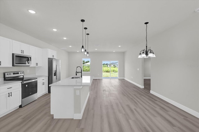 kitchen with sink, appliances with stainless steel finishes, a kitchen island with sink, and hanging light fixtures