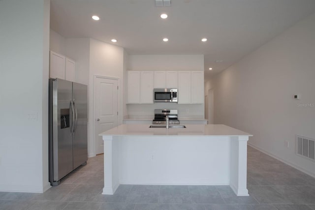 kitchen with white cabinets, an island with sink, stainless steel appliances, and light tile patterned flooring