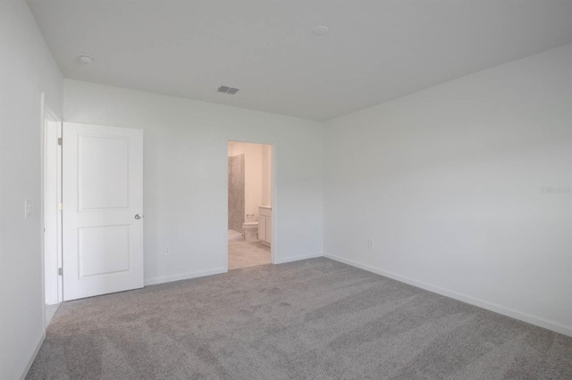 unfurnished bedroom featuring light colored carpet and ensuite bathroom