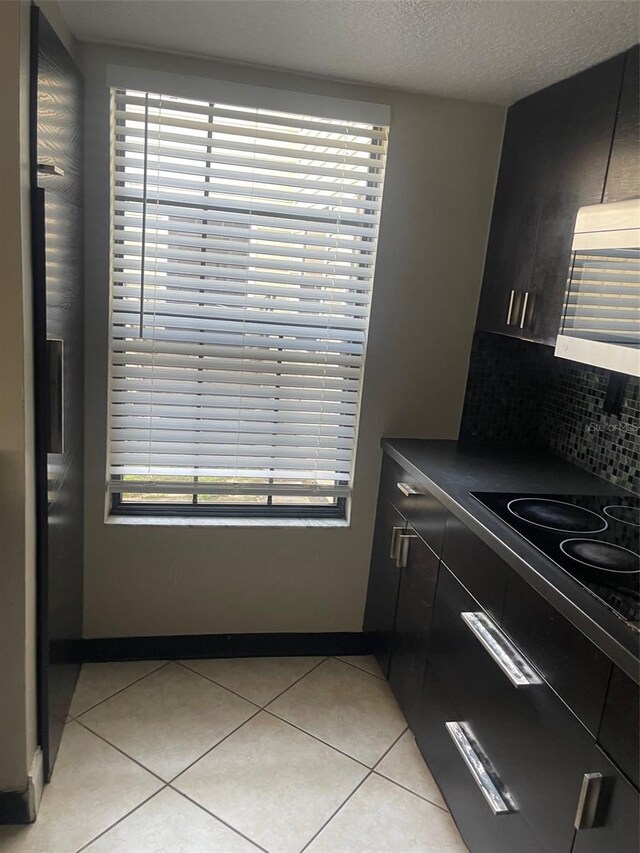 kitchen with dark countertops, light tile patterned floors, black electric cooktop, and decorative backsplash