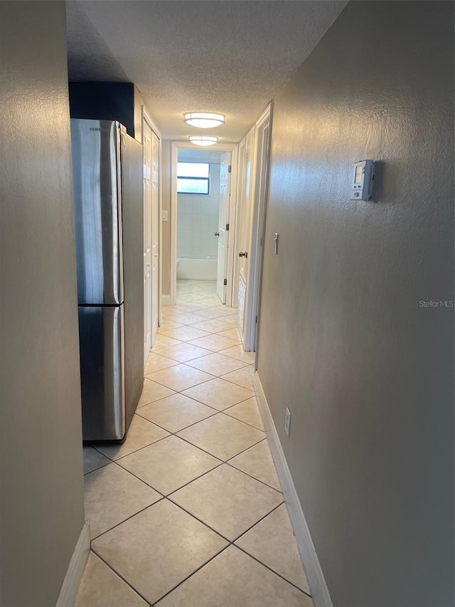 hall featuring light tile patterned flooring, a textured ceiling, and baseboards