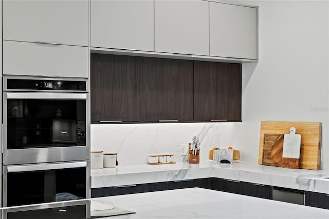 kitchen featuring light stone counters, white cabinets, tasteful backsplash, dark brown cabinets, and double oven