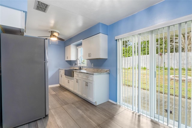 kitchen featuring stainless steel refrigerator, sink, ceiling fan, and white cabinetry