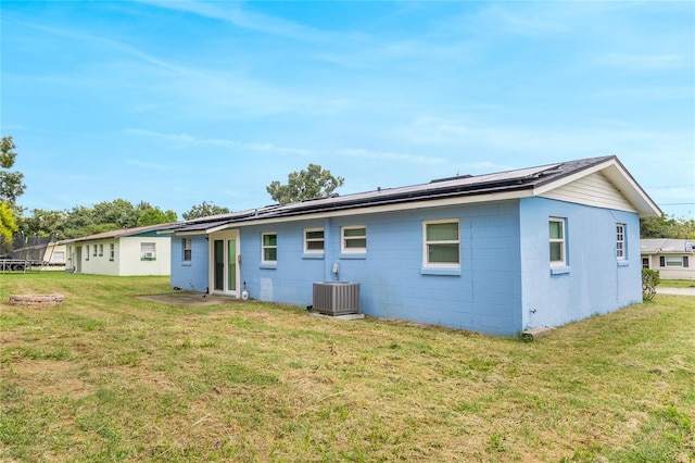 back of property featuring solar panels, cooling unit, a lawn, and a trampoline