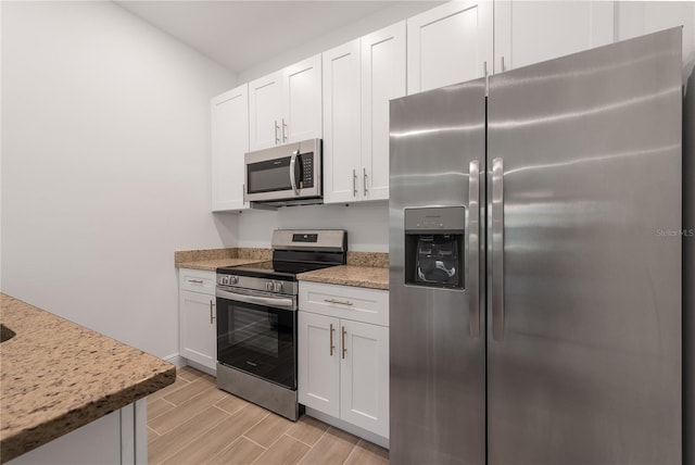 kitchen featuring light stone counters, appliances with stainless steel finishes, light wood-type flooring, and white cabinetry