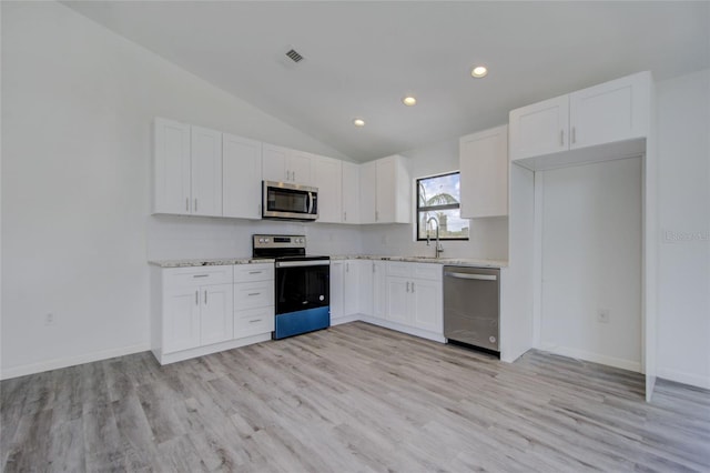 kitchen featuring light hardwood / wood-style floors, white cabinets, vaulted ceiling, appliances with stainless steel finishes, and light stone countertops