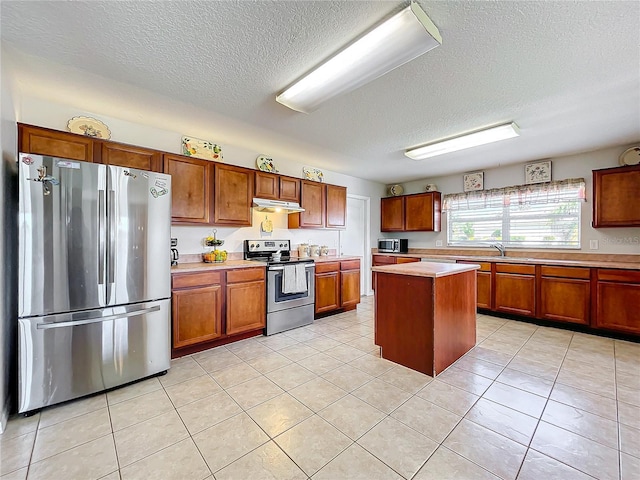 kitchen featuring a textured ceiling, brown cabinetry, light countertops, under cabinet range hood, and appliances with stainless steel finishes
