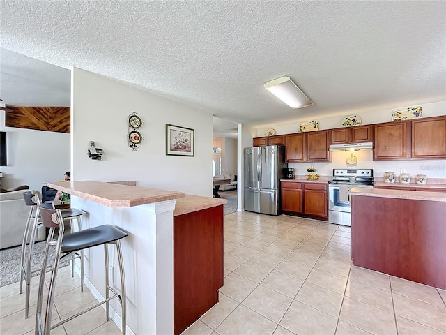 kitchen featuring a kitchen breakfast bar, a textured ceiling, appliances with stainless steel finishes, and light tile patterned flooring