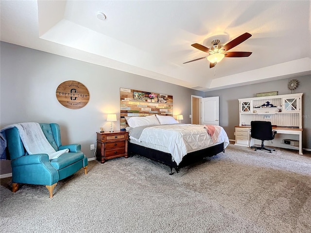 carpeted bedroom featuring a tray ceiling, a ceiling fan, and baseboards