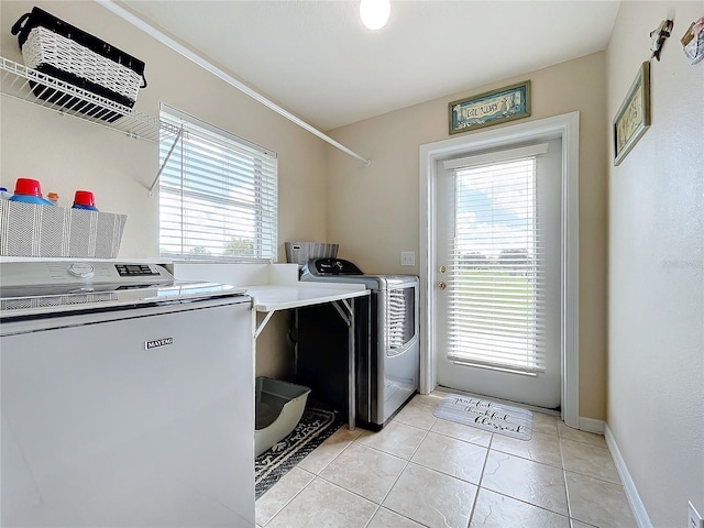 washroom with baseboards, washing machine and clothes dryer, light tile patterned floors, and laundry area