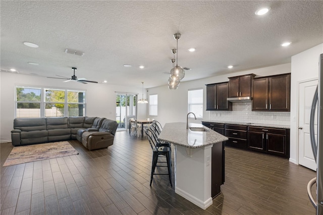 kitchen featuring a breakfast bar, dark wood-type flooring, sink, light stone countertops, and an island with sink