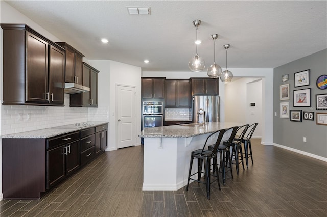 kitchen with dark hardwood / wood-style flooring, light stone counters, a center island with sink, and pendant lighting