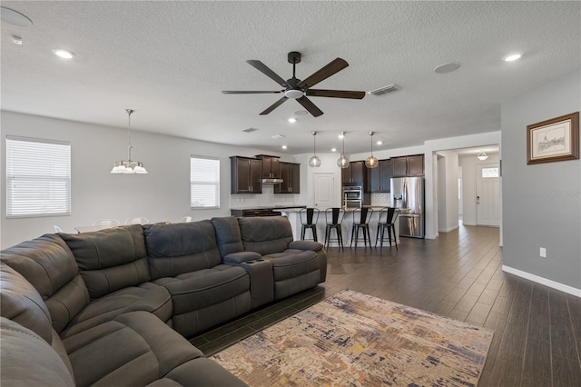 living room with ceiling fan with notable chandelier, dark wood-type flooring, and a textured ceiling