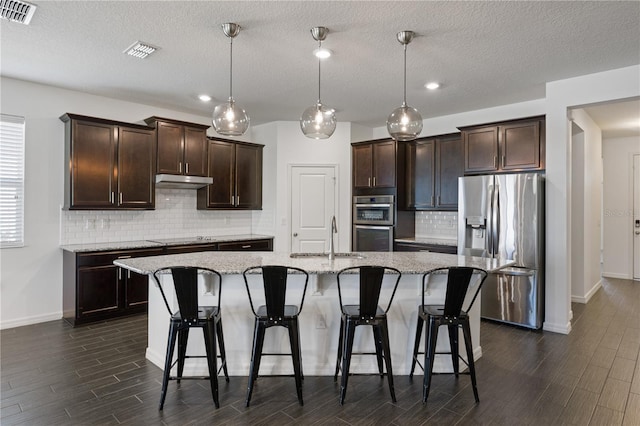 kitchen with light stone countertops, sink, pendant lighting, a center island with sink, and appliances with stainless steel finishes