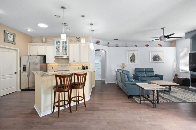 kitchen with ceiling fan, pendant lighting, an island with sink, stainless steel fridge, and a breakfast bar area