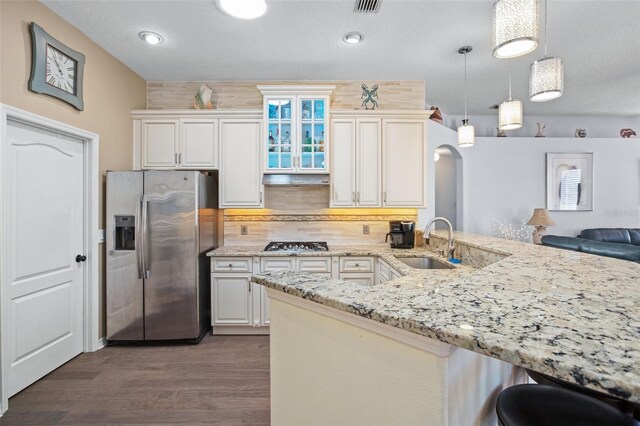 kitchen with hanging light fixtures, sink, kitchen peninsula, wood-type flooring, and stainless steel appliances