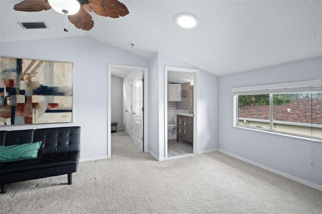 interior space featuring vaulted ceiling, light carpet, ceiling fan, and ensuite bathroom