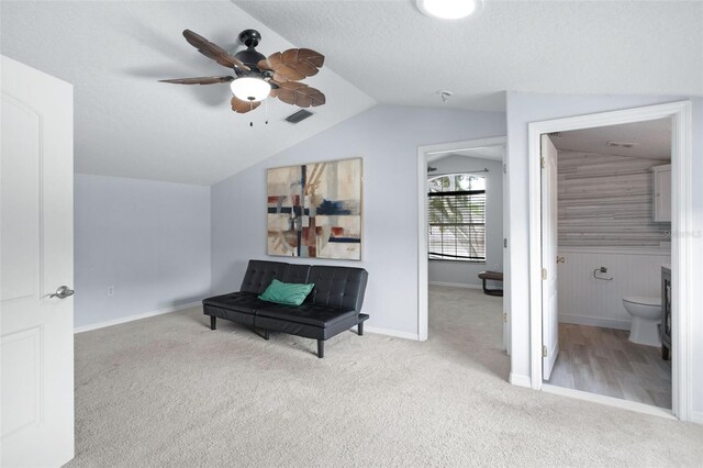 living area with vaulted ceiling, ceiling fan, light colored carpet, and a textured ceiling