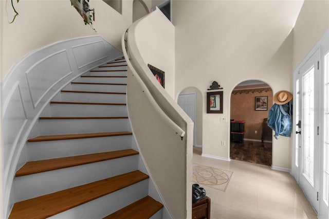 staircase with baseboards, a high ceiling, arched walkways, and tile patterned flooring