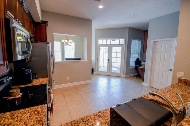 kitchen with light stone counters, light tile patterned floors, french doors, a chandelier, and range