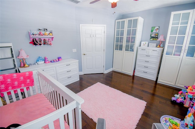 bedroom with ceiling fan, a nursery area, and dark hardwood / wood-style flooring