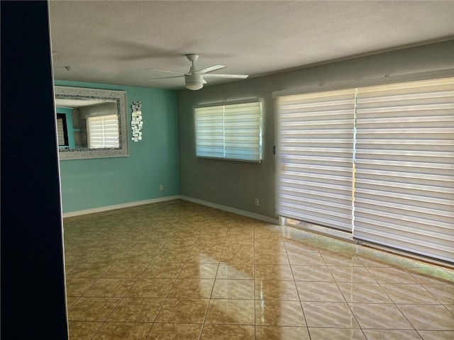 tiled spare room featuring a textured ceiling, ceiling fan, and baseboards